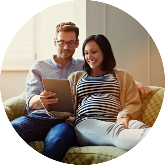 pregnant woman and her husband sitting on their sofa using a digital tablet